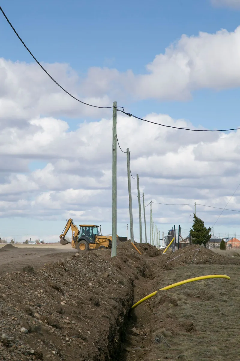Open utility trench with a yellow pipe beside a road lined with utility poles
